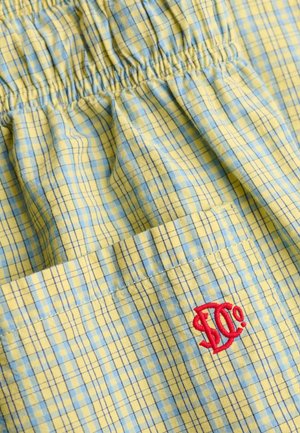 Tela de cuadros amarilla y azul con elástico fruncido y un logo rojo bordado "S. Co" en un bolsillo.
