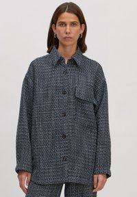 Große karierte Jacke in Marineblau und Weiß mit Kragen, Knopfverschluss vorne und einer einzelnen Brusttasche. Strukturierter Stoff.