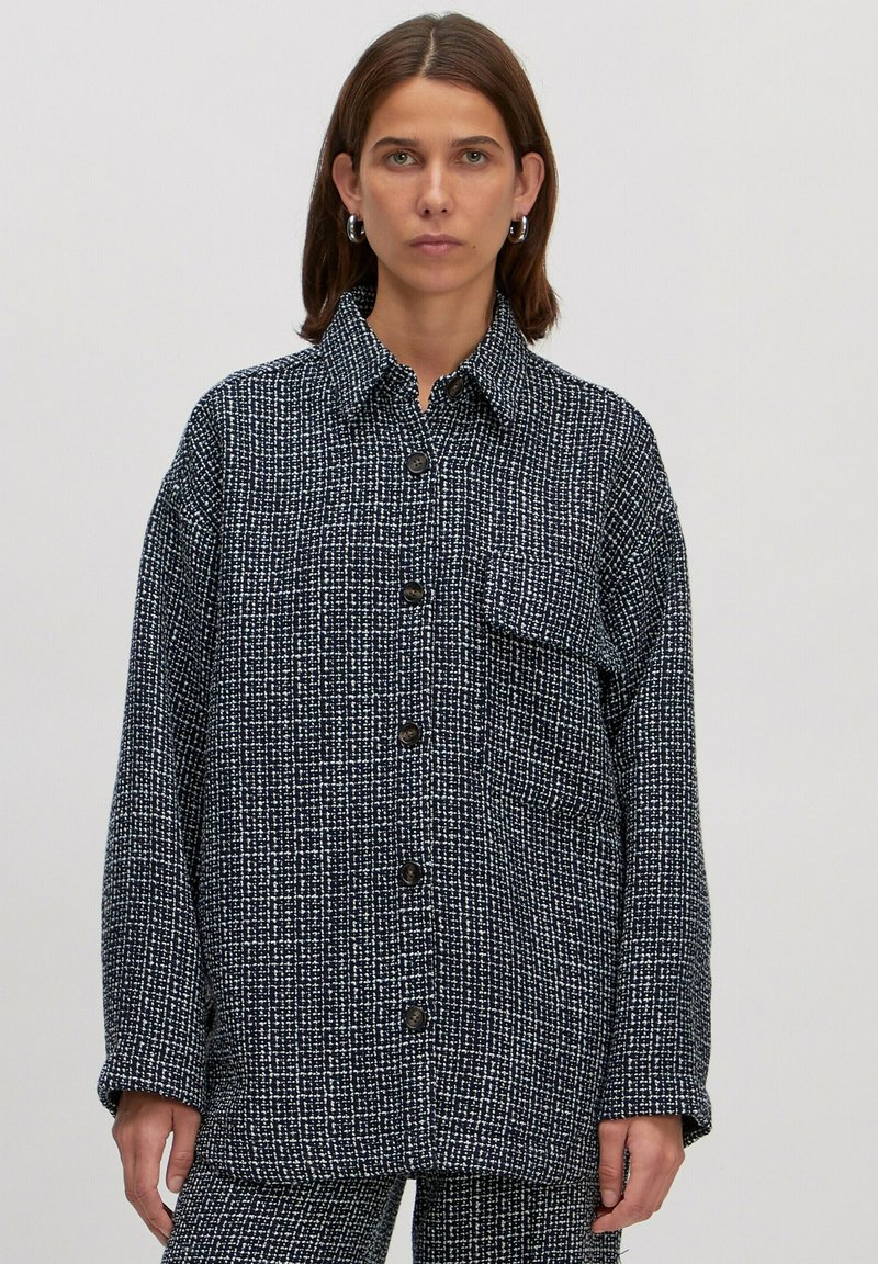 Große karierte Jacke in Marineblau und Weiß mit Kragen, Knopfverschluss vorne und einer einzelnen Brusttasche. Strukturierter Stoff.