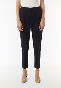 Navy gestreifte Hose mit taillierter Passform, ausgestattet mit einem mittelhohen Bund und schmal zulaufenden Beinen. Getragen mit beigefarbenen spitzen Absätzen.
