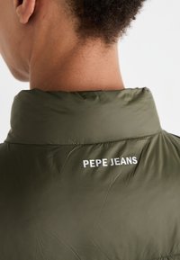 Olive spalvos švarkas su aukštu apykakle; ant nugaros yra baltas užrašas "PEPE JEANS"; lygus, lengvas audinio tekstūra.