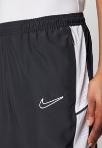 Crne Nike kratke hlače s elastičnom trakom, bijelim mrežastim bočnim panelima i bijelim izvezenim logotipom u donjem lijevom prednjem dijelu.