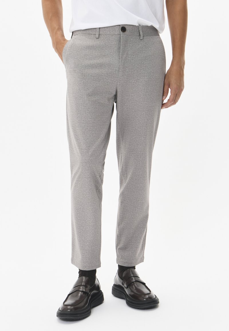 Pantalones de corte entallado en gris claro con una textura sutil, diseño de pierna recta y bolsillos delanteros, combinados con unos mocasines oscuros y pulidos.