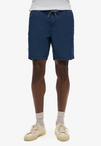 Pantalones cortos azul marino con un patrón texturizado, cinturilla elástica y cordón. Combinados con zapatillas y calcetines de color beige claro.