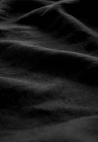 Gros plan d’un tissu noir avec une texture visible et des plis doux créant des ombres et des reflets.