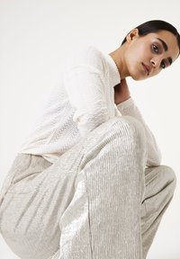 Witte textuurtrui met een chevronpatroon, gecombineerd met glanzende zilveren wijde broek. Beide stukken hebben een gladde, lichtreflecterende afwerking.