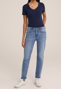 Marinblå V-ringad t-shirt och ljusblå rakbenjeans, med en klassisk femfickdesign och uppvikta nederkanter, ihop med vita sneakers.