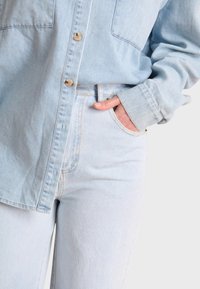 Camisa de mezclilla azul clara con dos bolsillos en el pecho, diseño de botones y mangas largas. Combinada con jeans azul claros a juego con un corte clásico.
