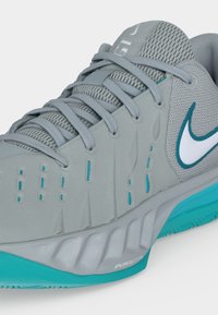 Γκρι και τιρκουάζ αθλητικό παπούτσι Nike για τρέξιμο με πλέγμα στο πάνω μέρος, κορδόνια και λευκό λογότυπο Swoosh στο πλάι, που δείχνει την μπροστινή και εξωτερική σόλα.