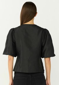 Blusa nera in satin con maniche corte a sbuffo, scollatura rotonda e silhouette aderente. Textura liscia con una leggera lucentezza.