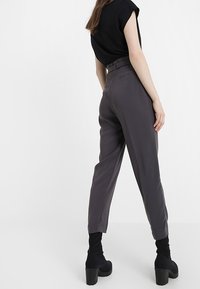 Szare spodnie w wysokim stanie o dopasowanym kroju, z subtelnym detalem paska i zwężanymi nogawkami, w połączeniu z czarnymi botkami za kostkę.