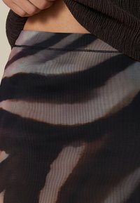 Gonna trasparente con motivo astratto marrone e nero. La vita è elasticizzata e il tessuto ha un aspetto leggero e testurizzato.