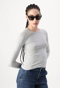 T-shirt gris à manches longues en matière douce, associé à un jean en denim bleu foncé. Lunettes de soleil noires angulaires et cheveux tressés stylés.