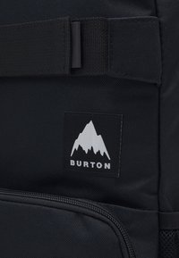 Zaino nero con tessuto texturizzato, una grande tasca con zip e un logo rettangolare con una montagna bianca e il testo "BURTON".