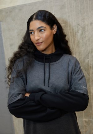 Grå og sort langærmet top med hætte, der har et sporty design og tekstureret stof. Inkluderer snore og logo på ærmet.