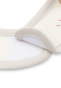 Close-up van een beige stoffen band met klittenbandsluiting die gedeeltelijk is losgehaald, waardoor de zachte stiksels en textuur zichtbaar zijn.