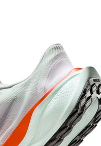 Nike hardloopschoen met een lichtgroene en witte bovenkant, rode accenten, gestructureerde stof en een gepatterneerde zwarte rubberen zool.