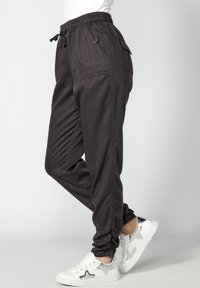 Pantalons de jogging gris foncé avec une taille élastique, des poches latérales et des poignet resserrés, associés à des baskets blanches avec des accents d'étoiles argentées.