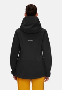 Svart vattentålig jacka med huva, med en slät yta. "Mammut"-logotypen tryckt i vitt på baksidan. Lämplig för utomhusbruk.