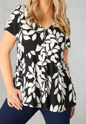 Blouse noire à motif de feuilles blanches, manches courtes, encolure en V, forme évasée, tissu texturé, portée avec un pantalon en denim foncé.