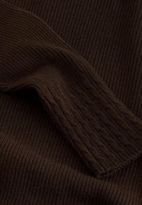 Tissu tricoté côtelé brun foncé avec une manche repliée montrant un motif torsadé texturé sur le poignet.