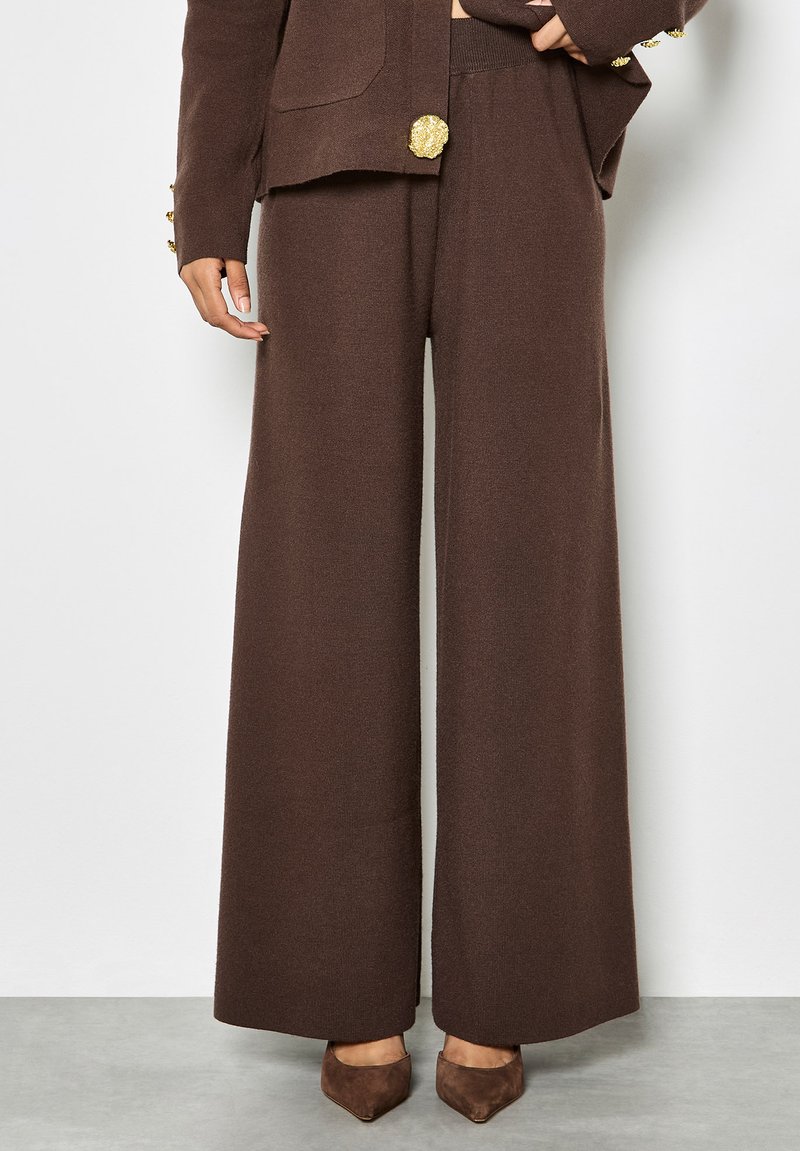 Braune Strick-Hosen mit weitem Bein und strukturiertem Finish, kombiniert mit einer passenden Jacke, die goldene Hardware-Akzente an den Bündchen und einen großen Knopf aufweist.