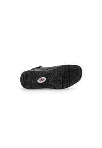 Semelle de chaussure noire avec un motif texturé, comportant des rainures circulaires et linéaires pour une meilleure adhérence. Petit logo rouge et blanc près du centre.