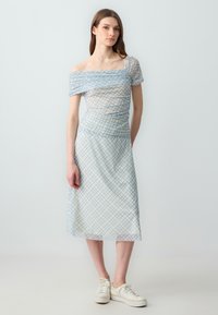 Abito scollato sulle spalle in un leggero motivo a quadri blu, con corpetto aderente e gonna fluida, abbinato a sneakers bianche.