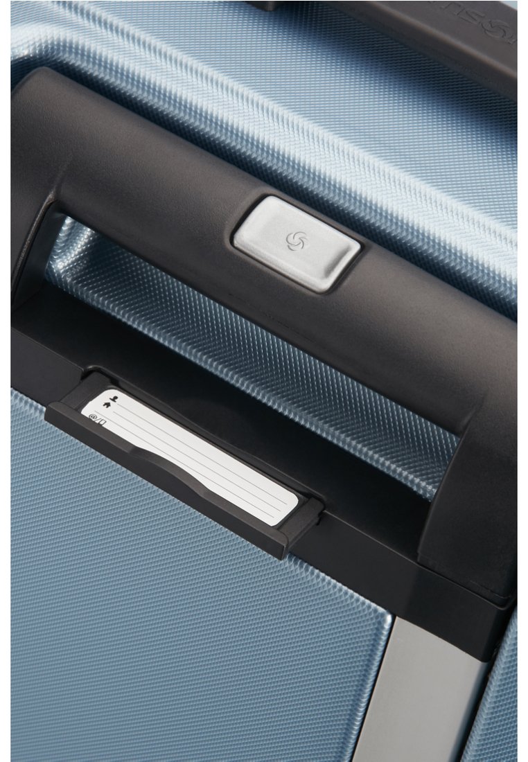 Poignée de valise rigide bleue avec une surface texturée et des accents noirs. Comprend un bouton en argent et un porte-carte pour identification.