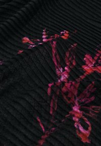 Tessuto nero testurizzato con un motivo arricciato, decorato con vivaci disegni floreali rosa e rossi, creando contrasto e profondità.