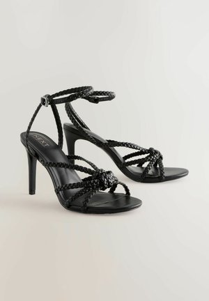 Sandale negre cu toc înalt, cu curele împletite, vârf deschis și cataramă la gleznă. Textură netedă, cu un design elegant și un toc subțire.