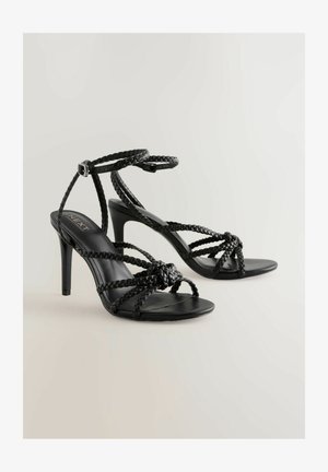 Sandali neri con tacco alto, dotati di cinturini intrecciati, apertura davanti e fibbia alla caviglia. Texture liscia con un design elegante e un tacco sottile.