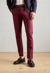 Bordeauxfarbene Slim-Fit-Hosen aus Baumwolle mit glatter Textur, kombiniert mit braunen Slippern mit goldenen Hardware-Details.