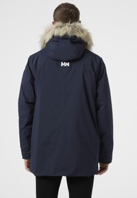 Námořnická modrá nepromokavá parka s kapucí z umělé kožešiny a detailem s logem. Mezi její funkce patří dlouhé rukávy, rovný střih a hladká textura.