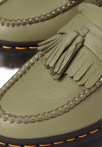 Oliwkowe skórzane mokasyny z frędzlami, teksturowanym przeszyciem i kontrastującą pomarańczową podeszwą.