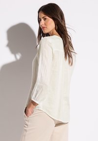 Blusa in lino leggera con maniche a tre quarti, scollatura a barca e vestibilità ampia. Presenta una sottile trama e un colore avorio attenuato.