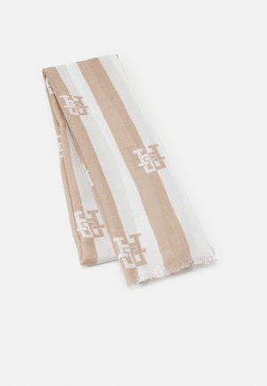 Tissu rayé beige et blanc plié avec un motif d'initiales abstraites répétées et des bords légèrement effilochés sur un fond uni.
