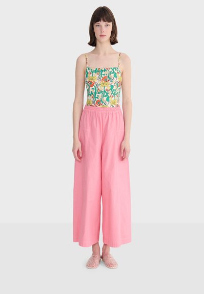 Femme portant un haut sans manches à fleurs avec de fines bretelles, un pantalon large rose ample et des chaussures plates tissées rose clair.