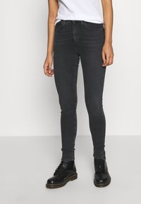 Černé úzké džíny s hladkou texturou, designem s pěti kapsami a šitými detaily, zkombinované s černými šněrovacími botami.