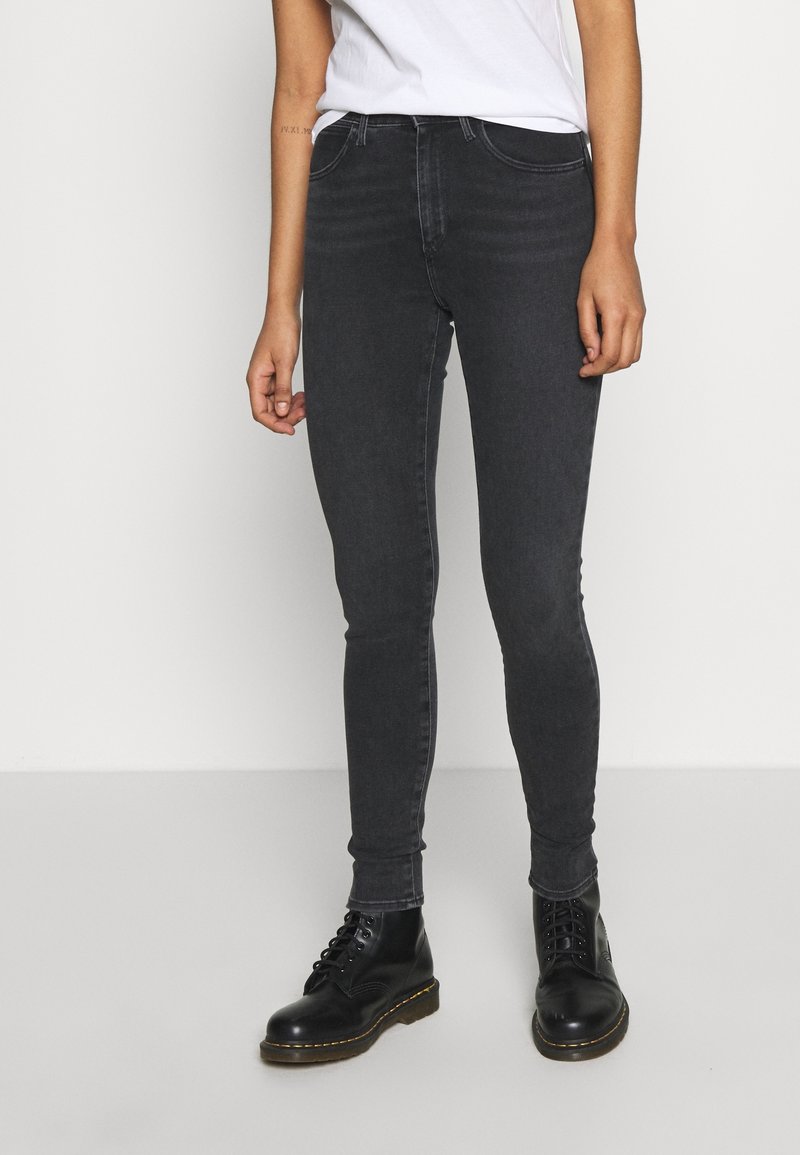 Černé úzké džíny s hladkou texturou, designem s pěti kapsami a šitými detaily, zkombinované s černými šněrovacími botami.