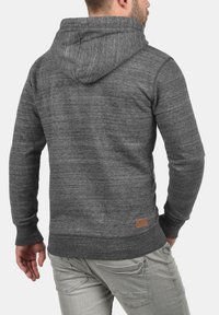 Grijze gemêleerde hoodie met een gestructureerde afwerking, capuchon met trekkoord en leren logo patch, gecombineerd met lichtgrijze broeken.