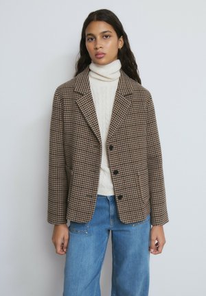 Braunes Hahnentritt-Sakko mit einreihigem Schnitt, Revers mit Kerbkragen und zwei Fronttaschen, getragen über einem cremefarbenen Pullover und blauen Jeans.