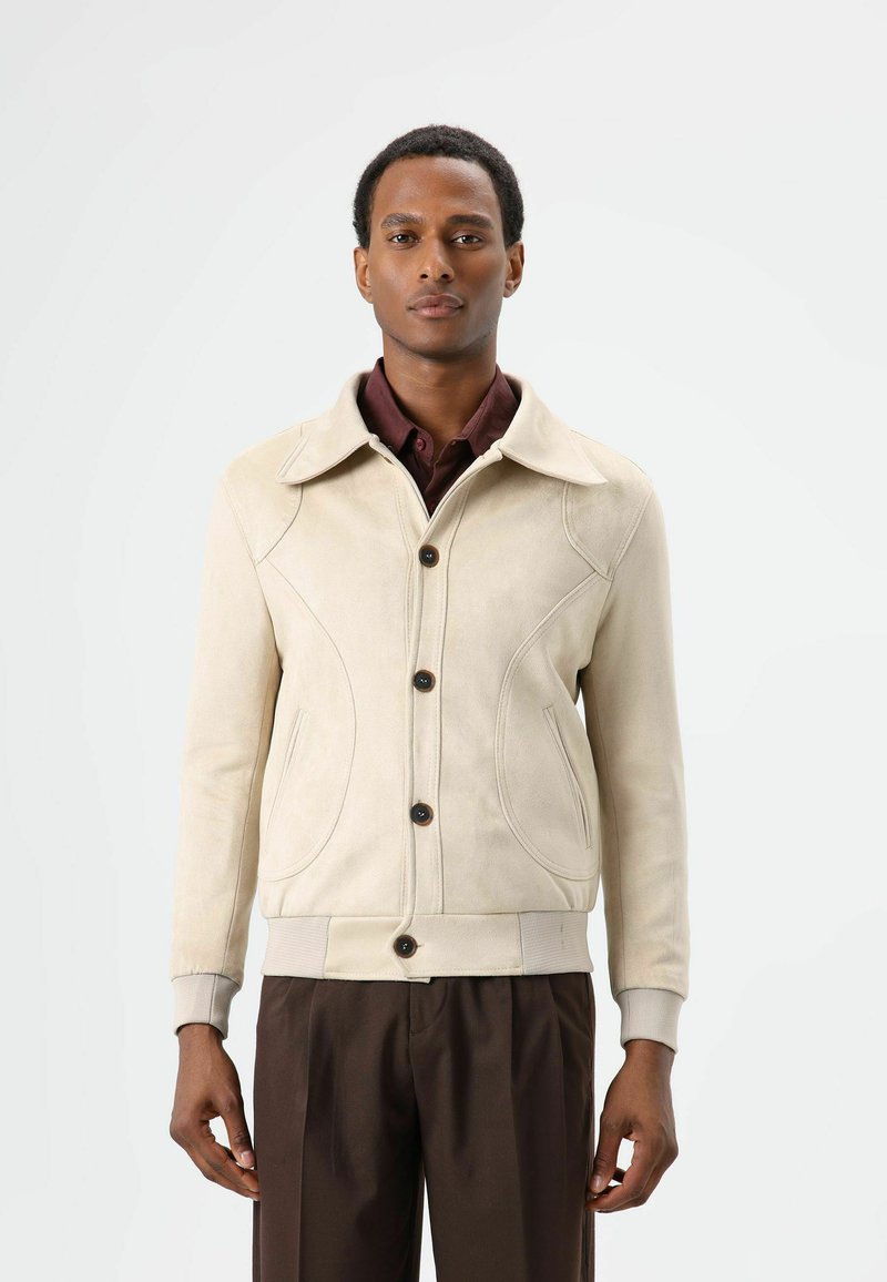 Beige suède jas met een gestructureerde kraag, knoopsluiting en decoratief stikwerk. Voorzien van zijzakken en geribde manchetten.