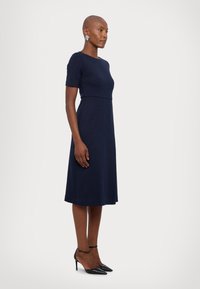 Tengerészkék, térdérő ruha rövid ujjakkal és testhez simuló felsőrésszel. Sima anyag, egyenes vonalvezetés, látható minták nélkül.