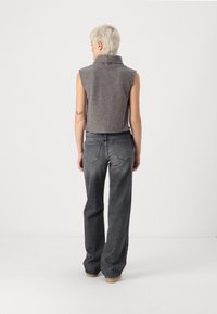 Grijze mouwloze trui met hoge kraag, gecombineerd met hooghals, ruime grijze jeans. Zachte textuur, comfortabele pasvorm. Minimale details.
