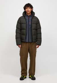 Dunjakke i olivengrøn med horisontal quiltning, gråt fleecefor, cargobukser i brun og sorte vandrestøvler med neonfarvede detaljer.