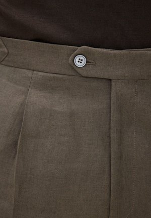 Lähikuva ruskeista kangashousuista, joissa on napillinen vyötärönauha ja näkyvät ompelusaumat.