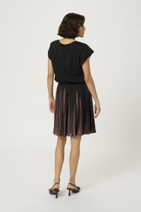 Haut à manches courtes noir associé à une jupe plissée de longueur genoux dans des nuances de brun foncé et clair. Les chaussures présentent des talons noirs.