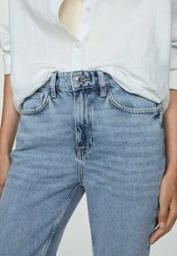 Light blue jeans with a high waist, visible front pockets, and a button closure. Material appears denim with subtle fading details.