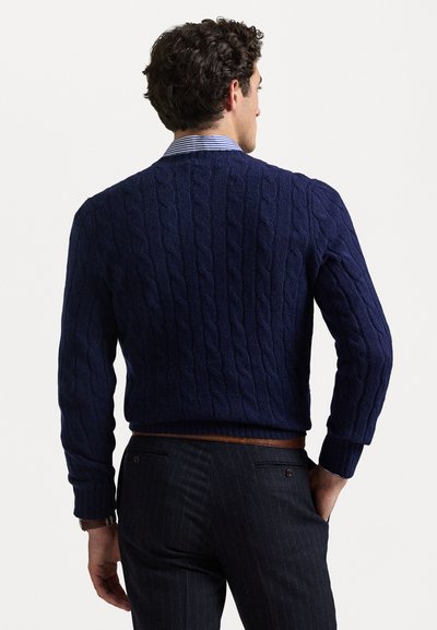 Pull en maille torsadée bleu marine avec un motif texturé, des poignets et une ceinture côtelés, associé à un pantalon à rayures et un col rayé.